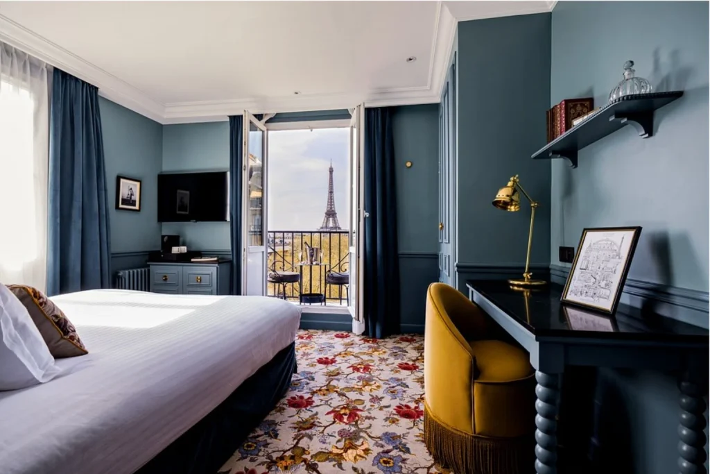 Elegant blue guest room with a private balcony framing a direct view of the Eiffel Tower at Hôtel Duquesne Eiffel in Paris.
