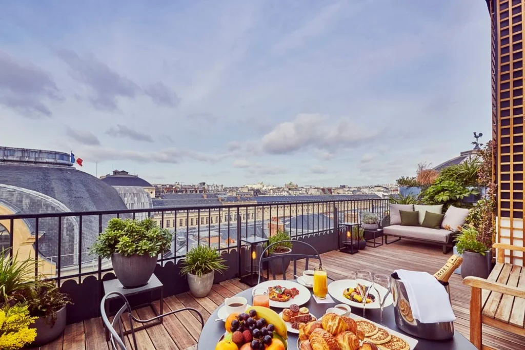 Beautiful rooftop terrace featuring a gourmet breakfast with fresh pastries, fruit, champagne, comfortable lounge seating and sweeping views over the Paris rooftops at Grand Hôtel du Palais Royal.