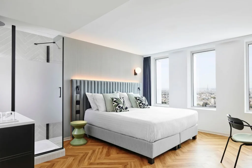 Modern double bedroom with floor-to-ceiling windows, panoramic Paris views, walk-in shower and wooden flooring at H4 Wyndham Paris Pleyel