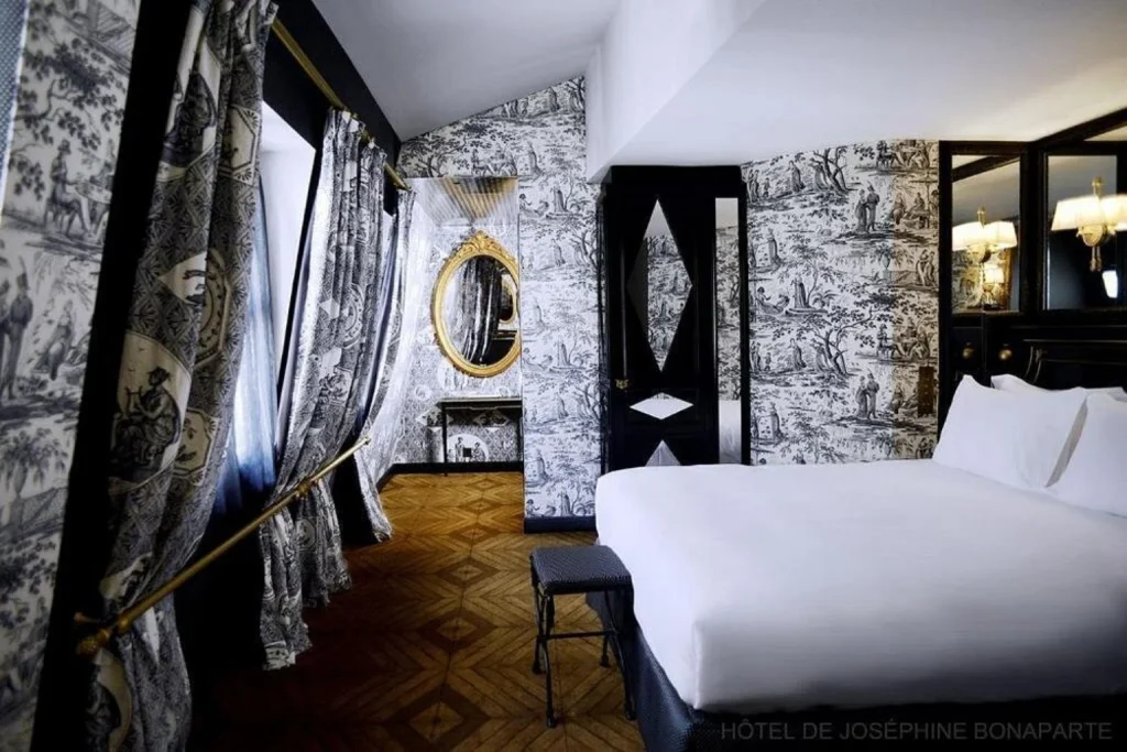 Elegant bedroom featuring dramatic black-and-white Toile de Jouy walls and curtains, parquet flooring and classic French details at Hôtel de JoBo Paris.