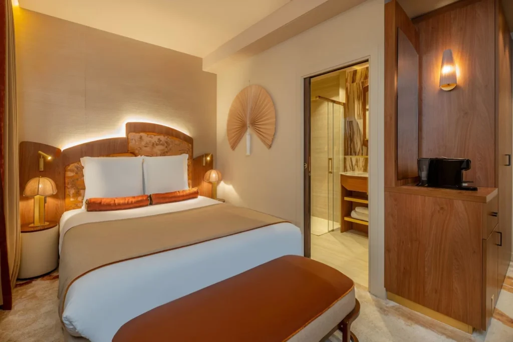 Warm contemporary bedroom with elegant wood details, soft lighting and an open ensuite bathroom at Hôtel de la Bourdonnais Paris.