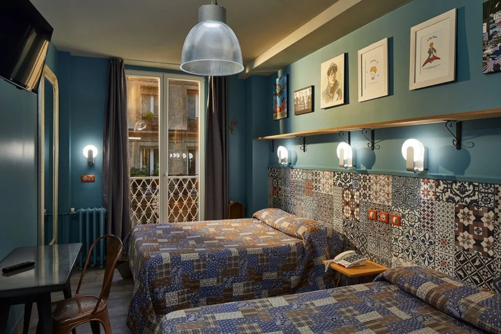 Charming boutique hotel room featuring two single beds, vibrant blue walls, intricate patterned tiles, vintage-style furniture and eclectic artwork at Hotel de Roubaix Paris.