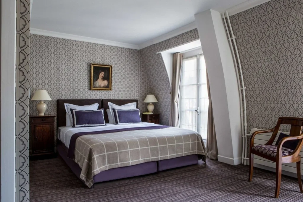 Classic bedroom with patterned wallpaper, purple accents and traditional furnishings at Hotel d'Orsay – Esprit de France Paris.