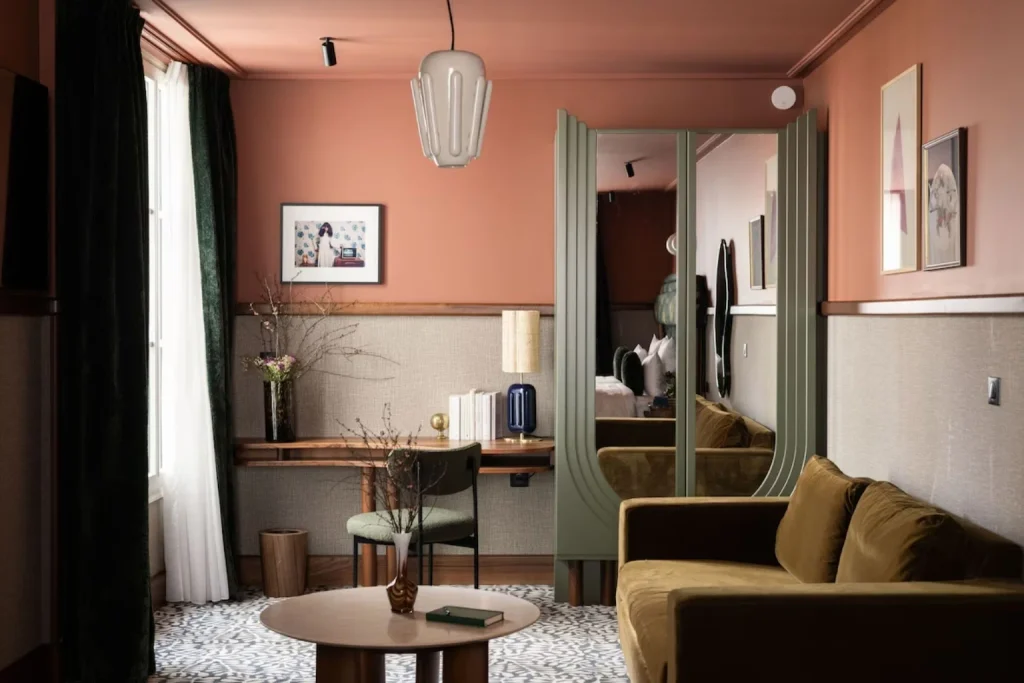 Stylish guest room with a comfortable sofa, work desk, statement mirrors and warm contemporary décor at Hotel La Trêve in Paris.