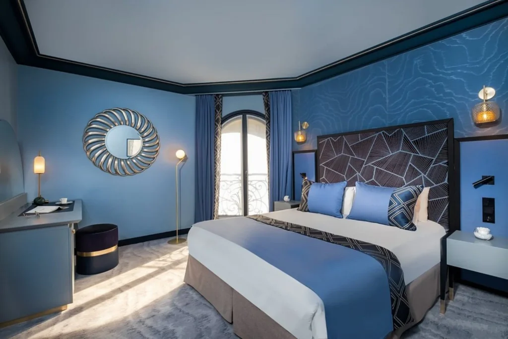 Stylish blue bedroom with a geometric headboard, modern lighting and elegant contemporary décor at Hôtel Le Derby Alma By Inwood Hotels Paris.