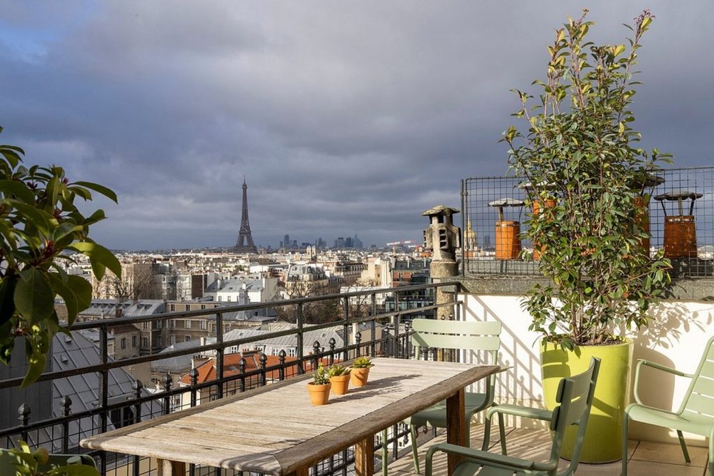 Private rooftop terrace with a wooden table, outdoor seating and panoramic views across the Paris skyline toward the Eiffel Tower at Hotel Le Littré Paris.