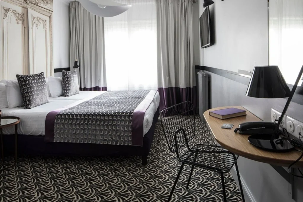 Stylish Parisian hotel room featuring a comfortable double bed, geometric patterned carpet, elegant wall detailing, a wooden desk and contemporary lighting at Hôtel Malte - Astotel.
