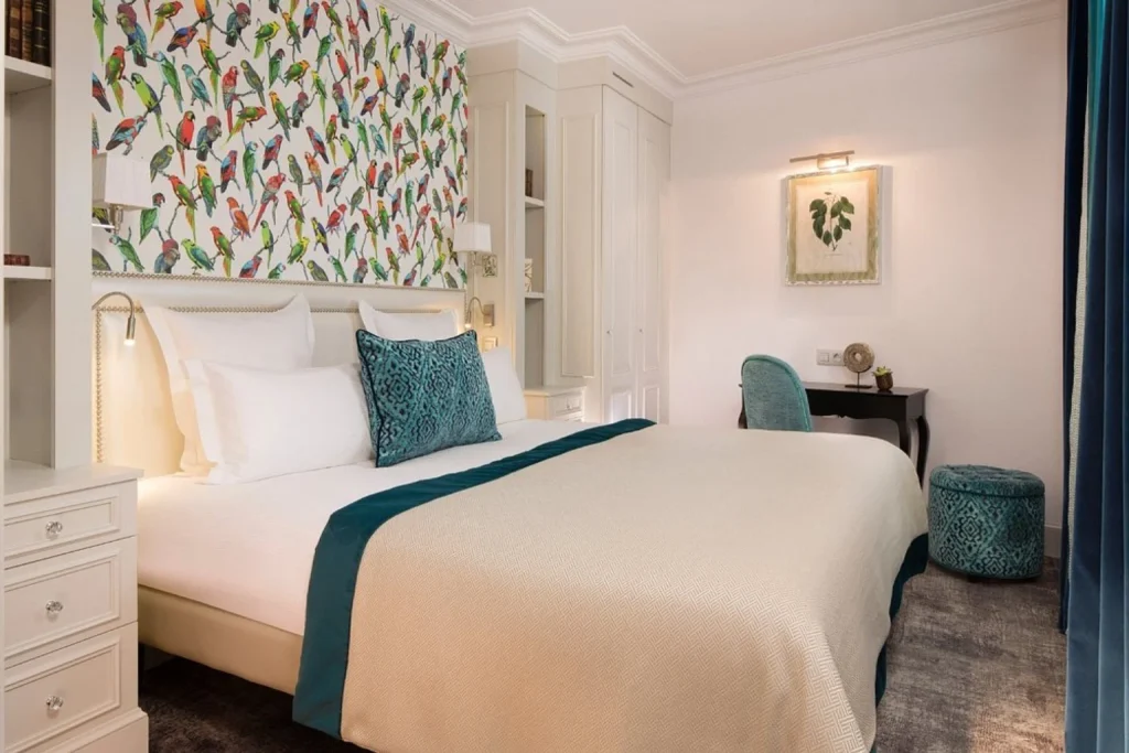 Stylish boutique hotel bedroom featuring vibrant tropical bird wallpaper, a comfortable double bed, turquoise decorative cushions and elegant furnishings at Hotel Monge Paris.