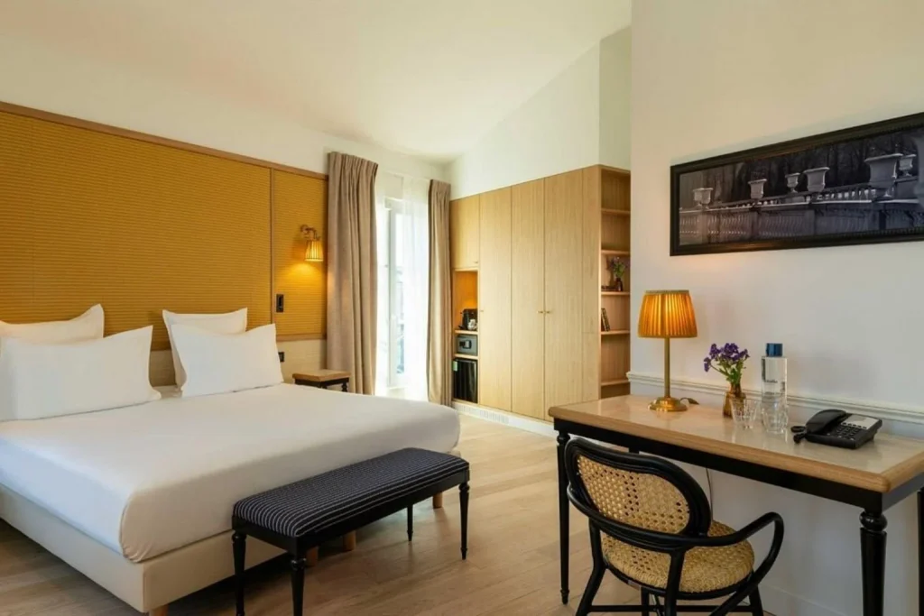 Bright contemporary bedroom with warm wooden furnishings, a large bed and elegant writing desk at Hôtel Observatoire Luxembourg Paris.