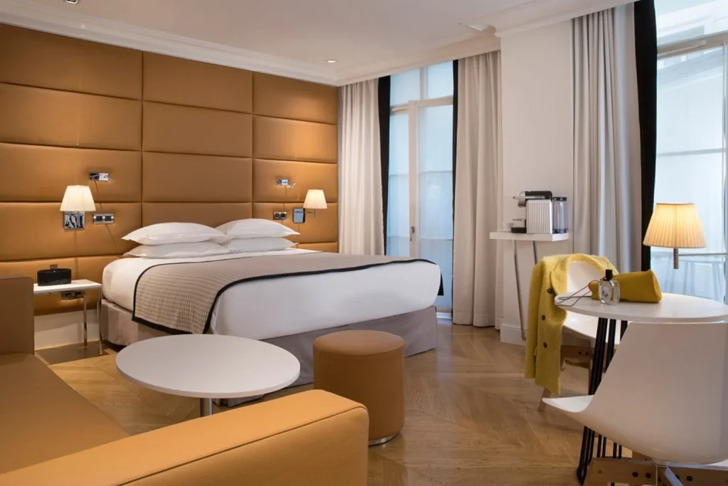 Bright and spacious hotel room featuring a comfortable double bed, upholstered beige headboard, contemporary seating area, wooden flooring and elegant lighting at Hôtel R de Paris.