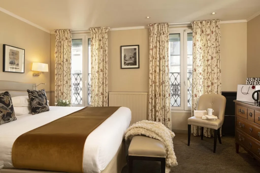 Warmly decorated bedroom with floral curtains, classic furnishings and a spacious double bed at Hotel Relais Bosquet By Malone Paris.