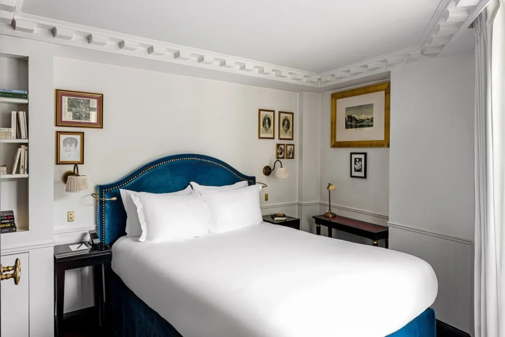 Elegant boutique hotel room with a blue velvet headboard, classic French details and framed artwork at La Chambre du Marais, Paris, France