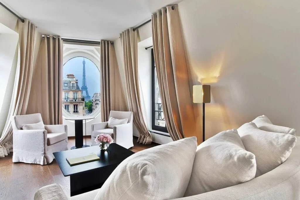 Bright contemporary living room with white seating and a distinctive round window framing the Eiffel Tower at Le Metropolitan, Paris Tour Eiffel.