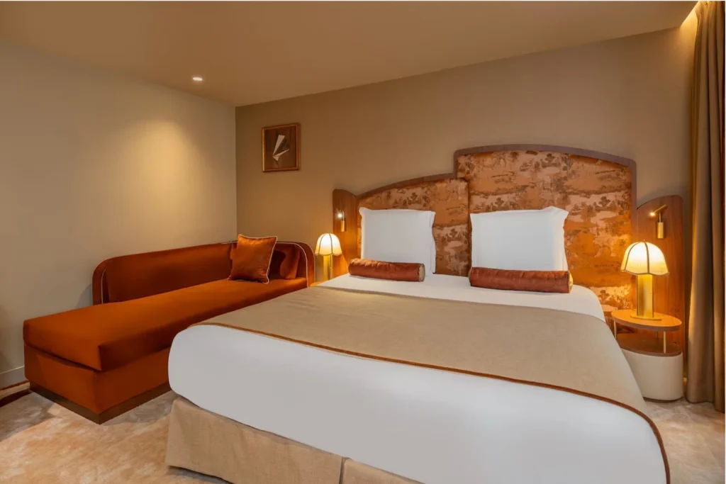 Warmly styled guest room with a sculptural upholstered headboard, elegant lighting and a comfortable lounge sofa at La Bourdonnais in Paris.