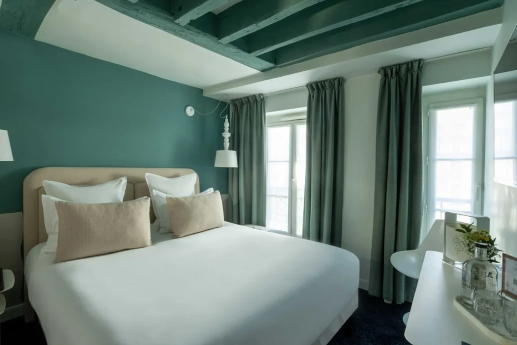 Bright boutique hotel room with a comfortable double bed, exposed wooden beams and calming green interiors at MARAIS HÔme Hotel, Paris, France