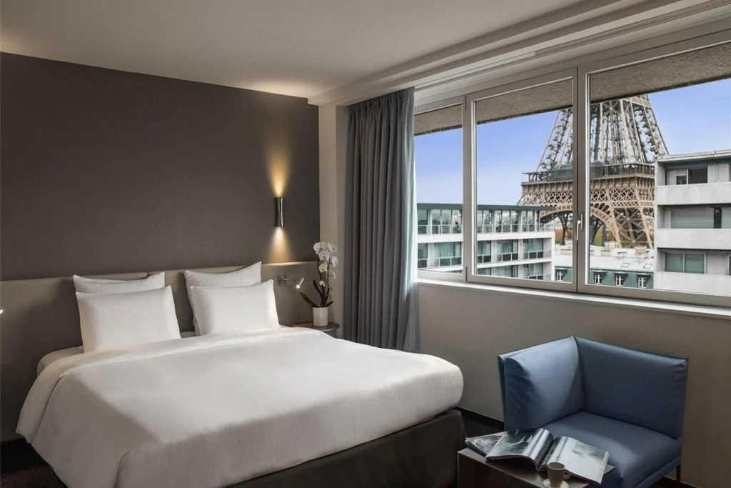 Modern bedroom with floor-to-ceiling windows offering a striking close-up view of the Eiffel Tower at Pullman Paris Tour Eiffel.