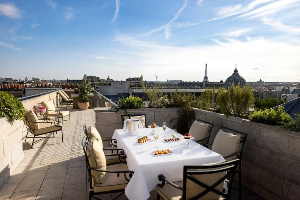 Exclusive rooftop terrace featuring an elegant outdoor dining area, champagne, lush greenery and spectacular views of the Eiffel Tower and Paris skyline at Ritz Paris.