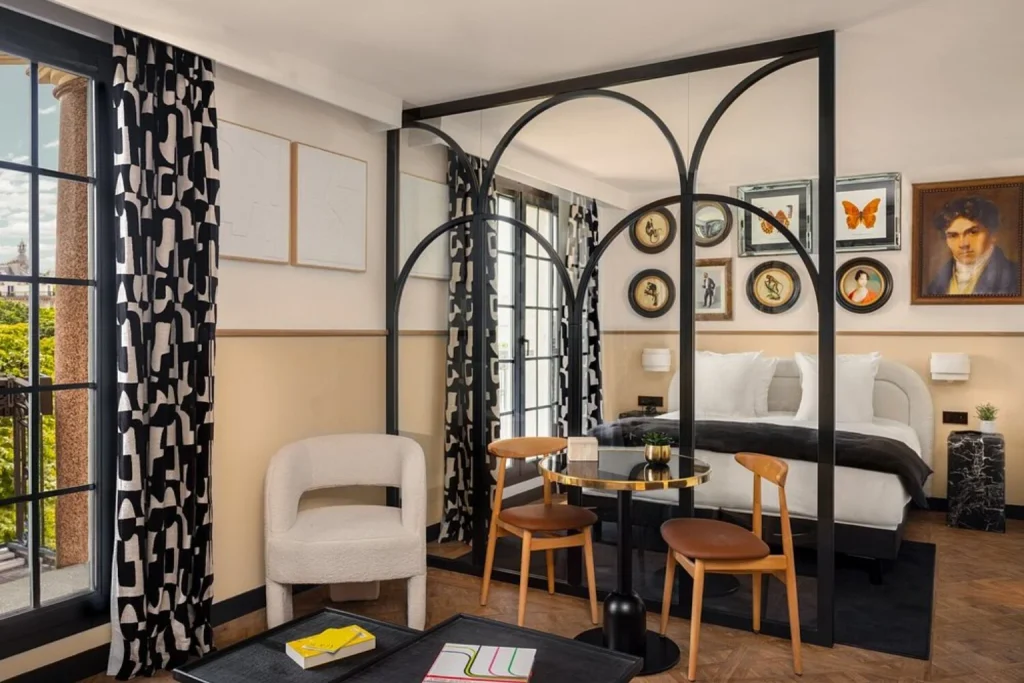 Stylish hotel suite with glass partition, double bed, geometric curtains, contemporary furniture and artistic wall decor at Solly Hôtel Paris