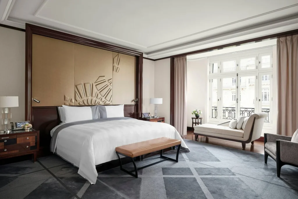 Spacious luxury bedroom with a king bed, elegant seating area and large windows overlooking Paris at The Peninsula Paris