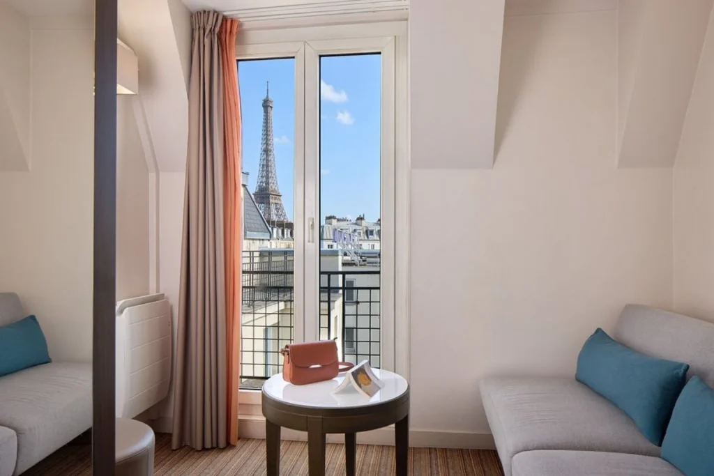 Bright sitting area with a sofa and large window framing a close view of the Eiffel Tower at Timhotel Tour Eiffel Paris.