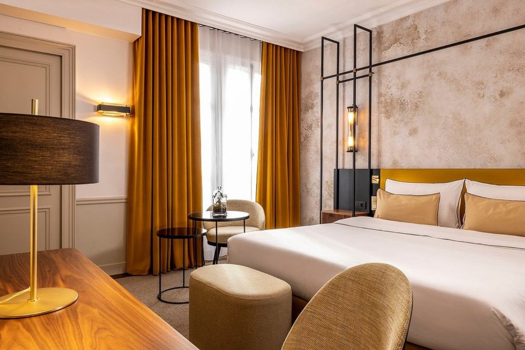 Elegant double bedroom with mustard yellow curtains, white bedding, textured walls and contemporary lighting at Victoria Palace Hotel Paris